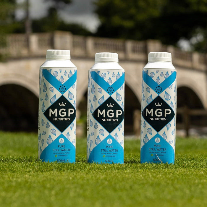 MGP Nutrition Pure Still Water 24 x 500ml. 3 Bottles on grass with a bridge out of focus in the background.