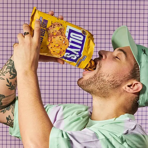 Olly's multi-seed pretzel thins being poured into mouth by man wearing cap