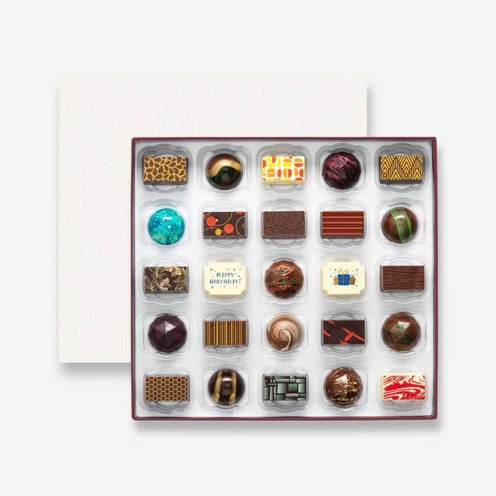 An open chocolate selection box containing 25 chocolates made by Harry Specters. The chocolates seen within this gift box are a colourful mix of white, milk, and dark chocolate with two Happy Birthday message chocolates.