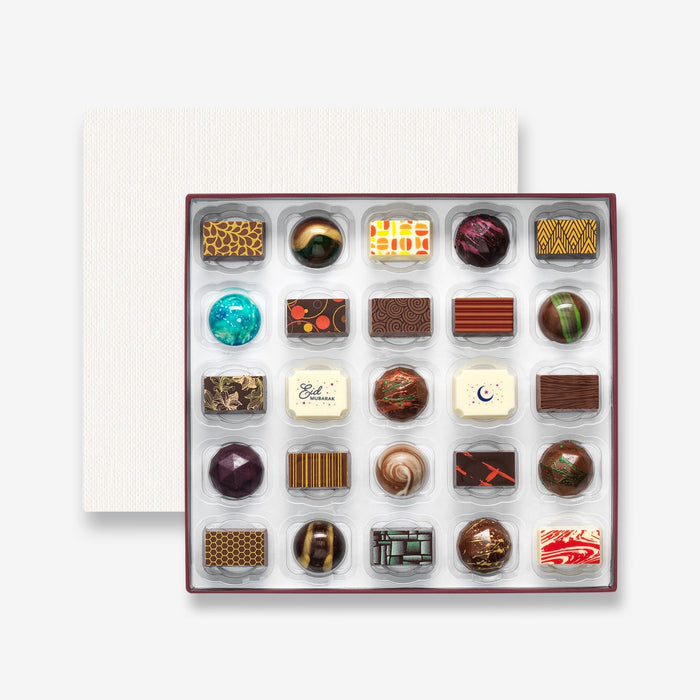 An open chocolate selection box containing 25 chocolates made by Harry Specters. The chocolates seen within this gift box are a colourful mix of white, milk, and dark chocolate with two Eid Mubarak message chocolates.