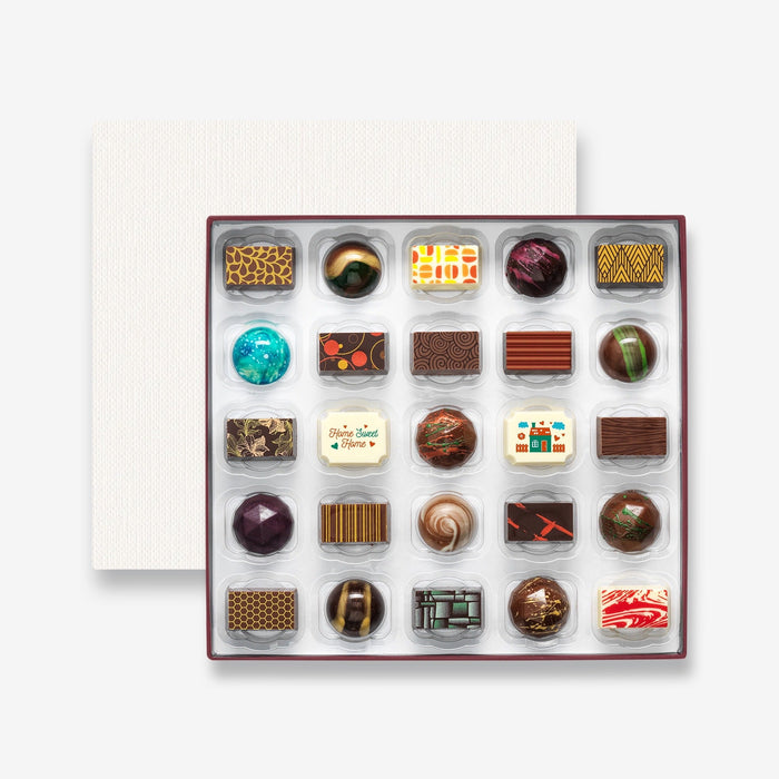 An open chocolate selection box containing 25 chocolates made by Harry Specters. The chocolates seen within this gift box are a colourful mix of white, milk, and dark chocolate with two New Home message chocolates.