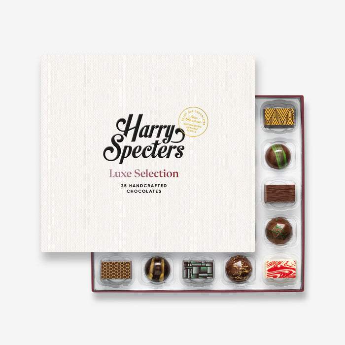 A chocolate selection box containing 25 chocolates, partially covered by a lid showing the name Harry Specters. The chocolates seen within this gift box are a colourful mix of white, milk, and dark chocolate with two New Home message chocolates.