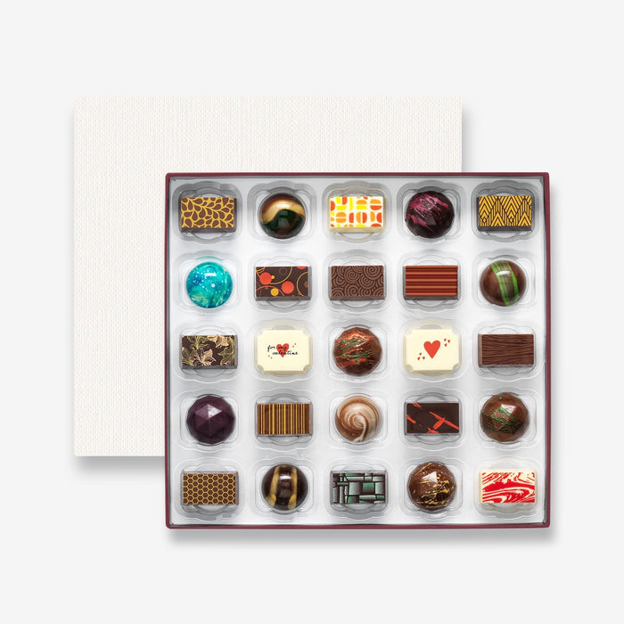 An open chocolate selection box containing 25 chocolates made by Harry Specters. The chocolates seen within this gift box are a colourful mix of white, milk, and dark chocolate with two Valentine's Day message chocolates.