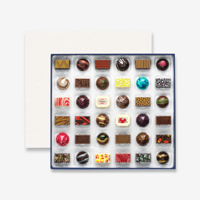 An open chocolate selection box containing 36 chocolates made by Harry Specters. The chocolates seen within this gift box are a colourful mix of white, milk, and dark chocolate with two Mother's Day message chocolates.
